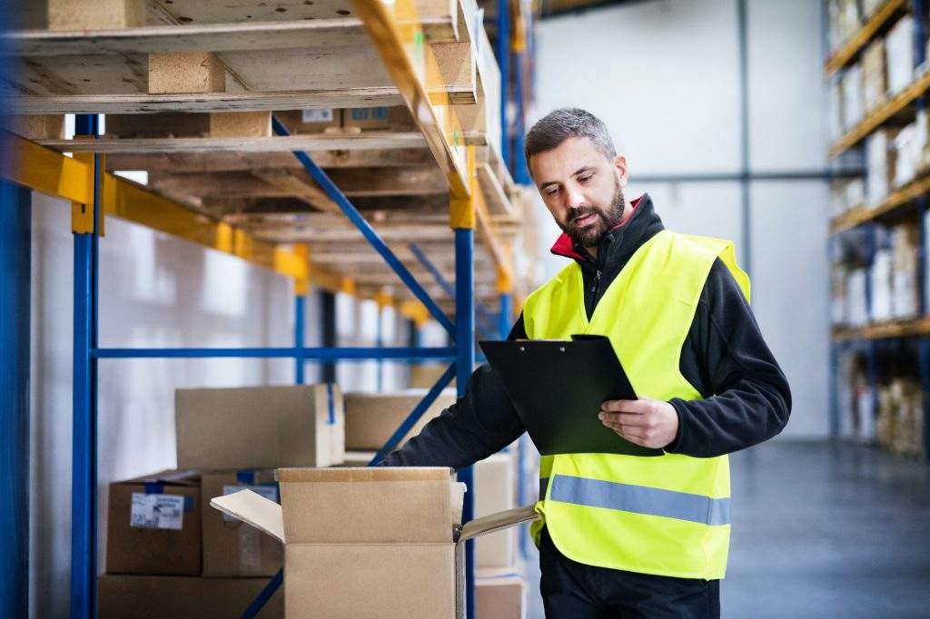 A man in a yellow vest is looking at a clipboard